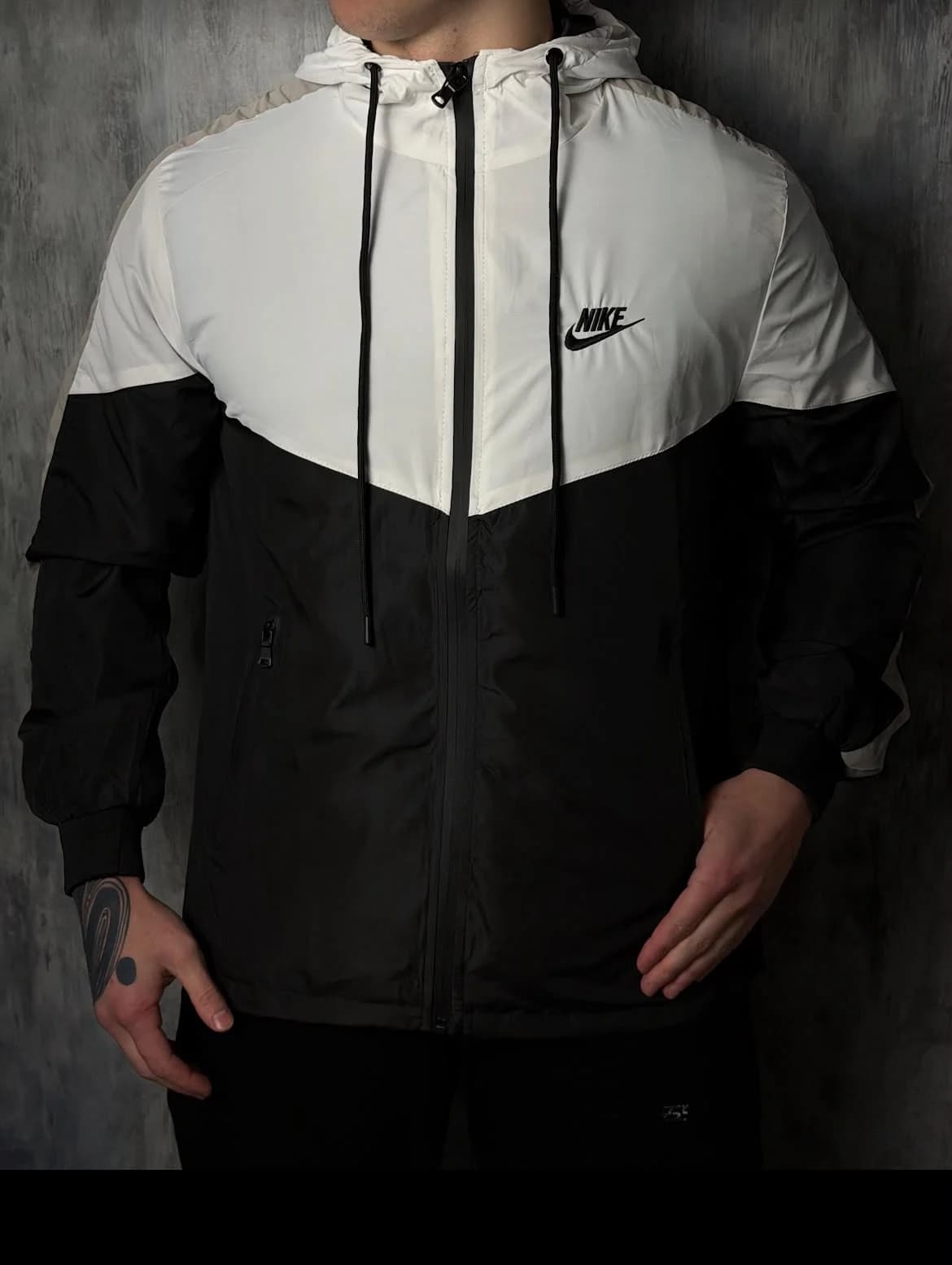 Corta vento Nike preto e branco vestido, na frente de um muro de concreto